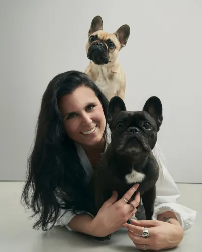 Una creator abbraccia due bulldog francesi, uno in braccio e uno sulla spalla