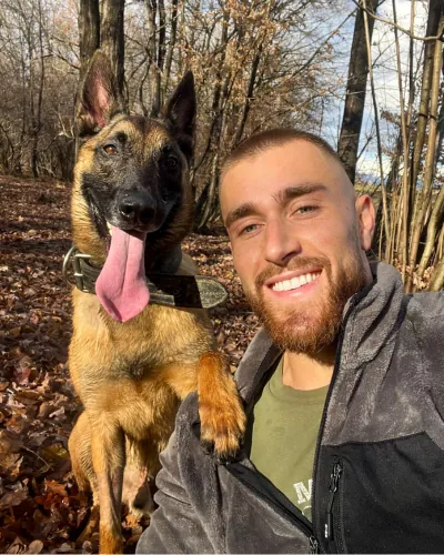 Gabriele sorride accanto a Drake, pastore belga malinois, nel bosco