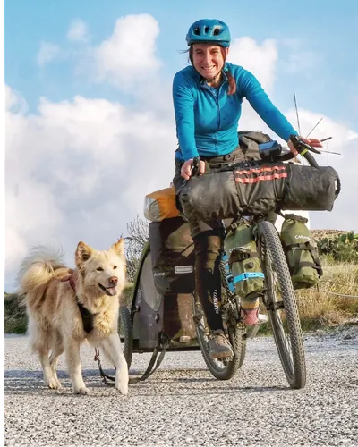 Veronica in bicicletta da viaggio carica di borse, con Nala al suo fianco